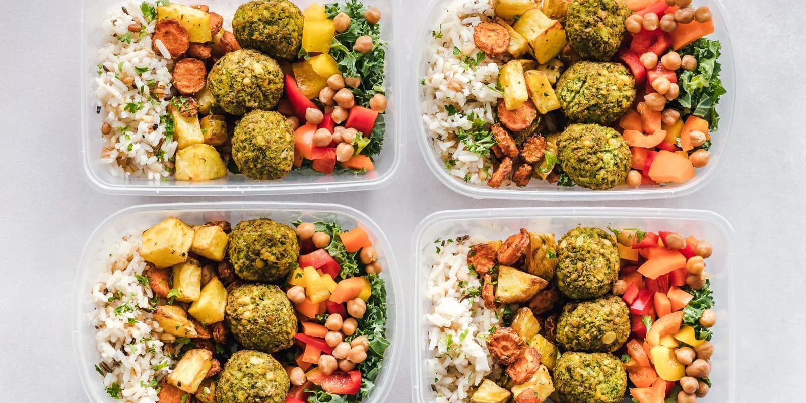 Four meal prep containers with rice, vegetables and falafel seen from above