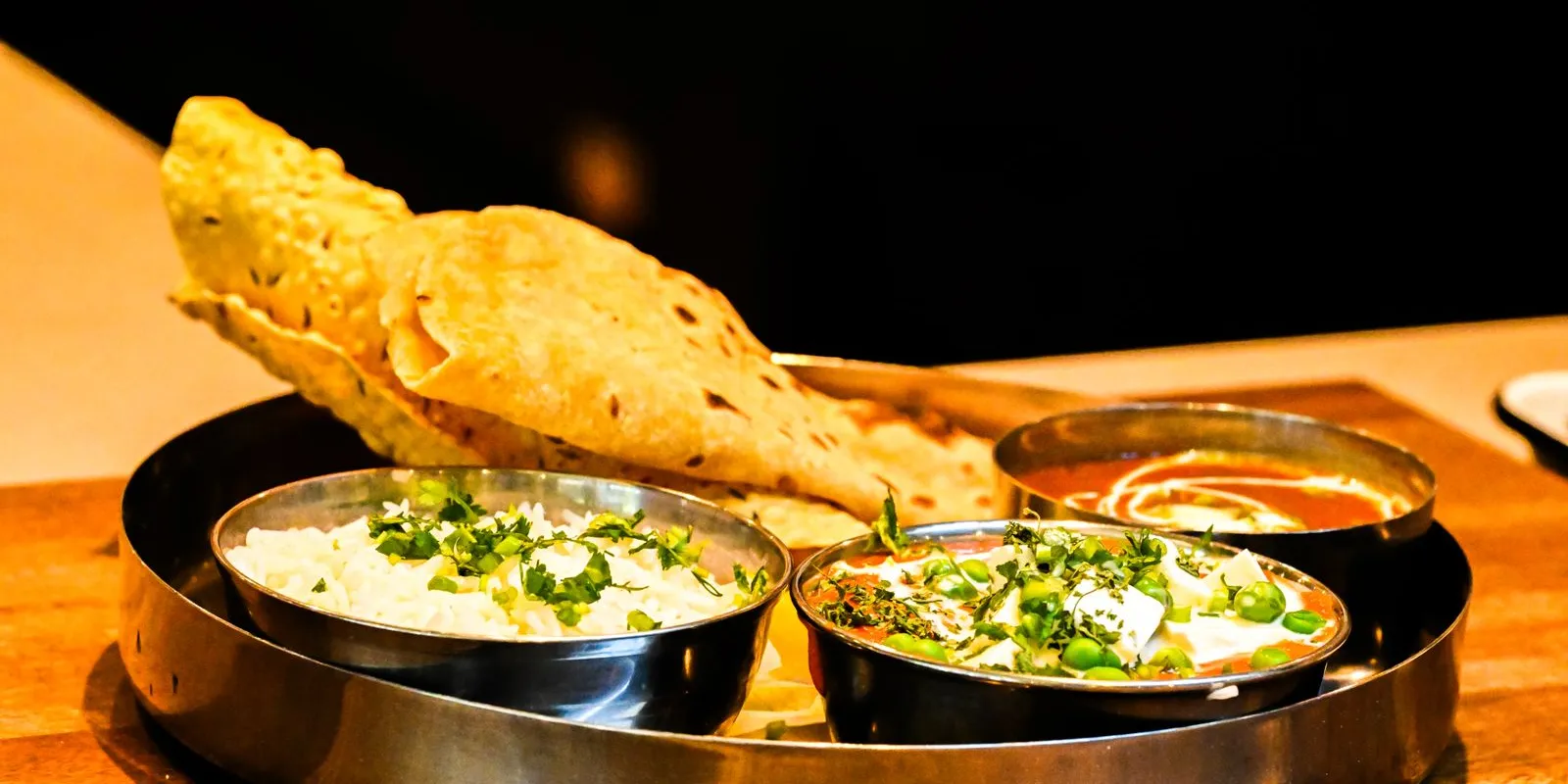Indian thali with paneer curry, dal and papad on a steel tray