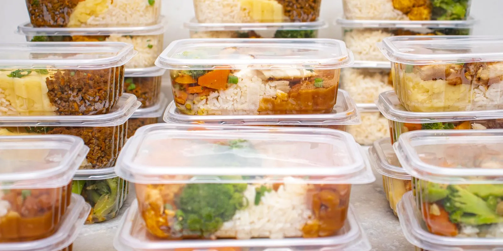 Stacked meal prep containers filled with rice, vegetables and sauce