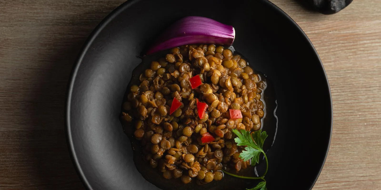 Cooked brown lentils with red onion and parsley on a black plate