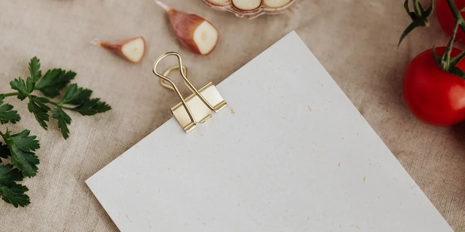 Blank sheet of paper on a clipboard surrounded by garlic, tomatoes and parsley
