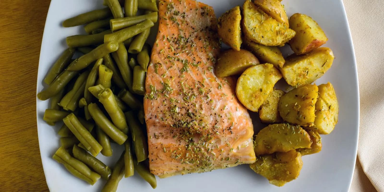 Baked salmon fillet with roasted potatoes and green beans on a white plate