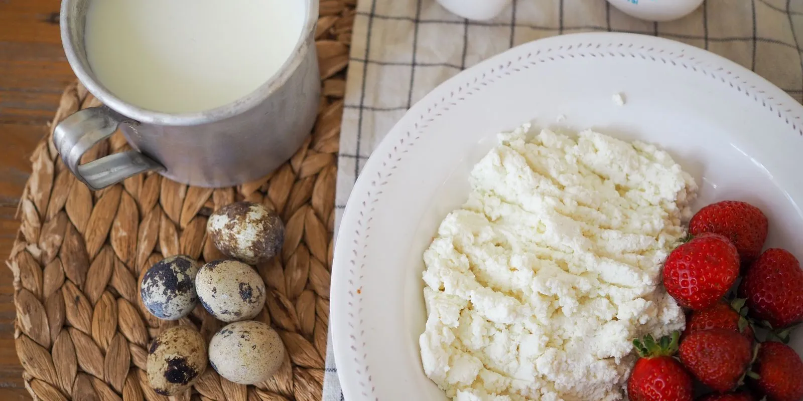 Cottage cheese with strawberries on a plate next to a mug of milk